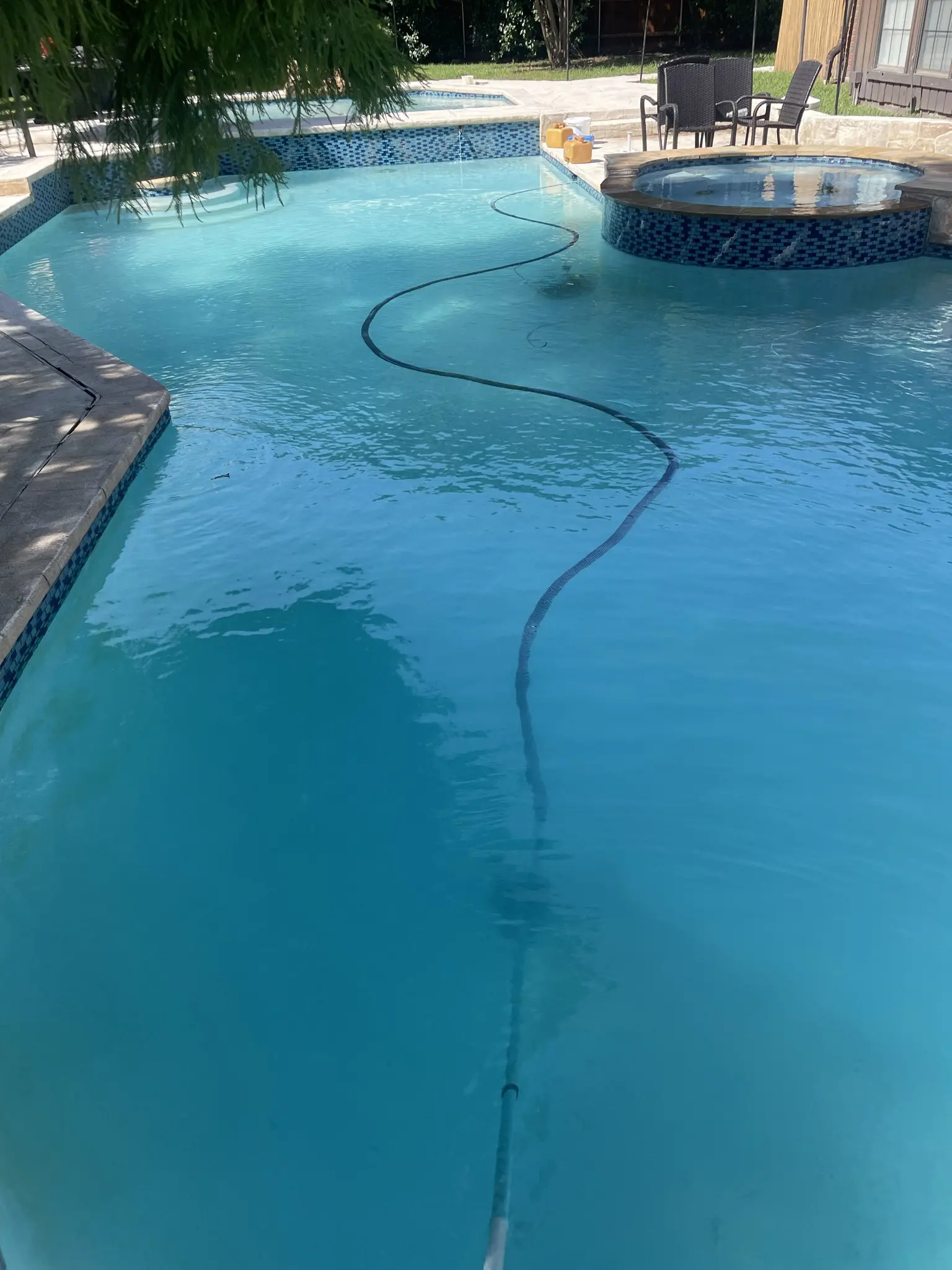 A clear turquoise pool with a raised round spa faced in blue mosaic tile spilling into the main pool.