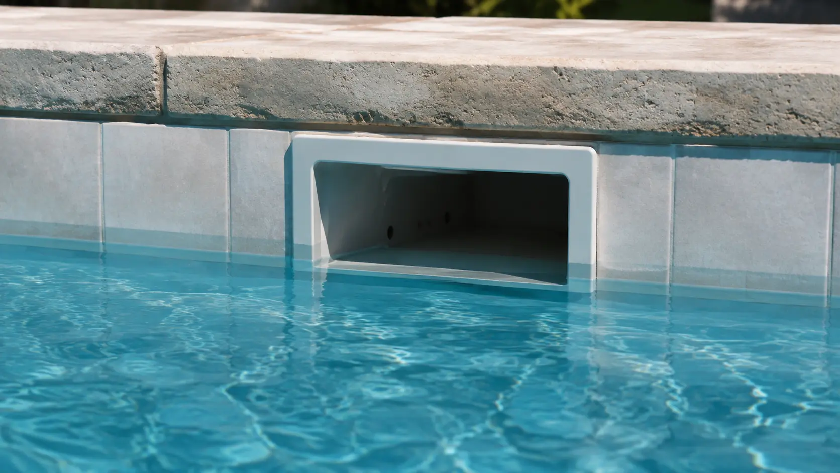 A swimming pool skimmer opening set into the tiled pool wall, with the water level fallen below the bottom of the opening and a band of dry tile exposed above the waterline.