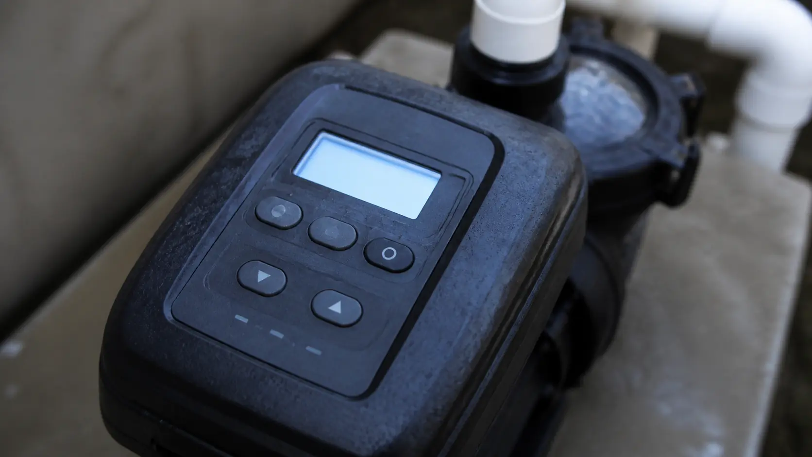 A close view of the backlit control keypad on top of a modern variable speed pool pump on a concrete equipment pad.