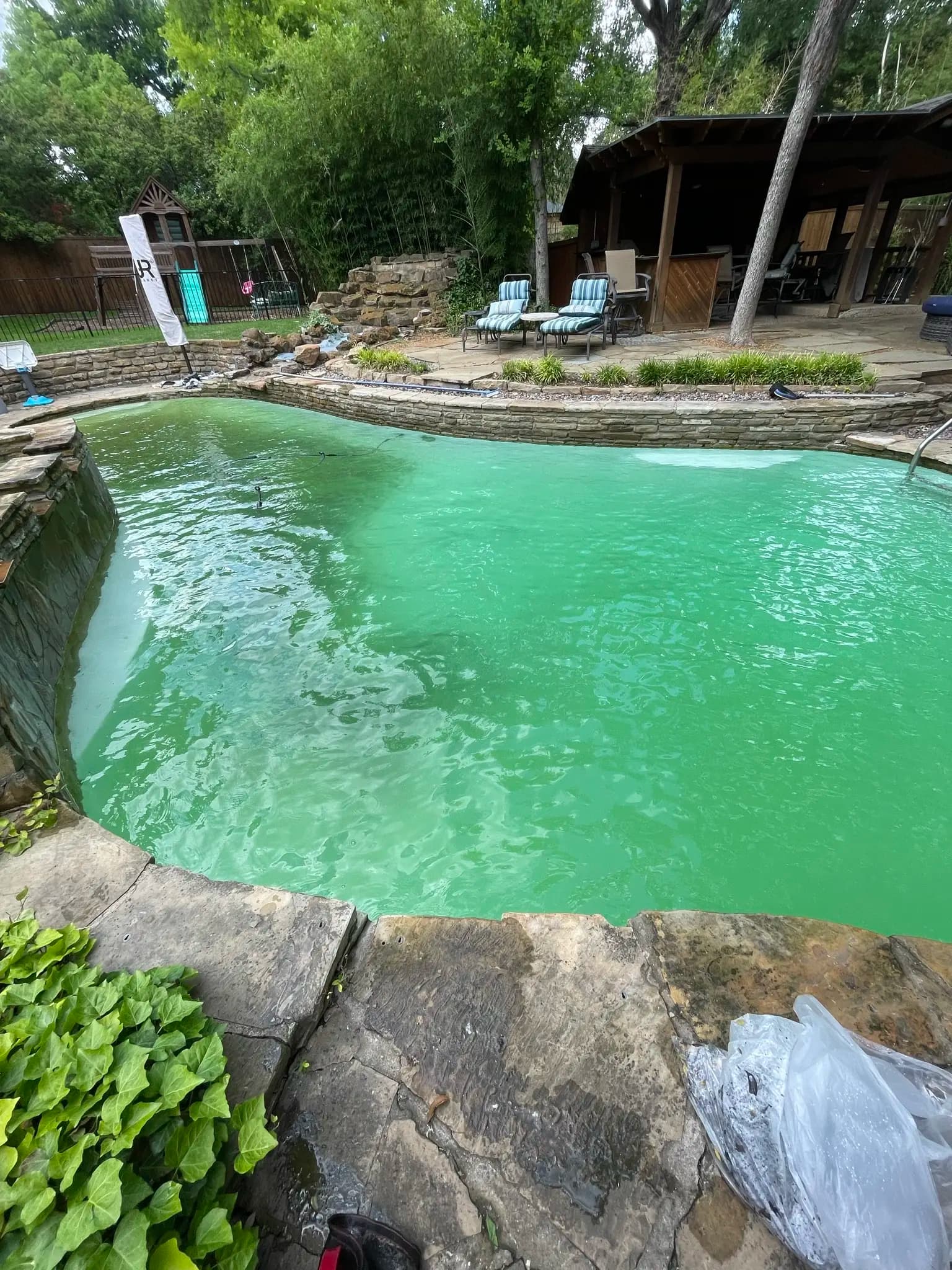 Green pool water against stone coping and a flagstone deck
