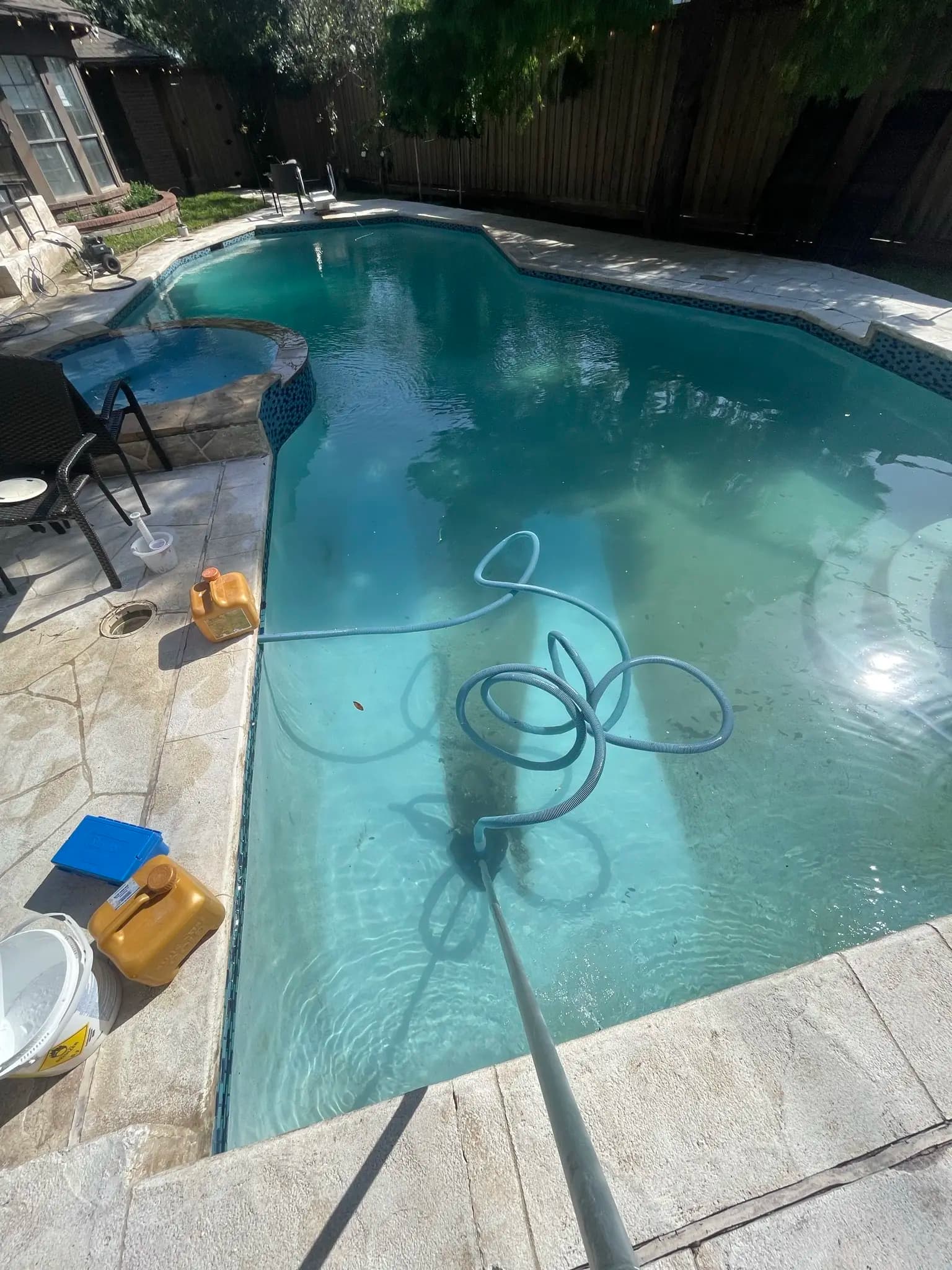 The same pool part way through a clean, water turning from green to cloudy blue with a vacuum hose across it