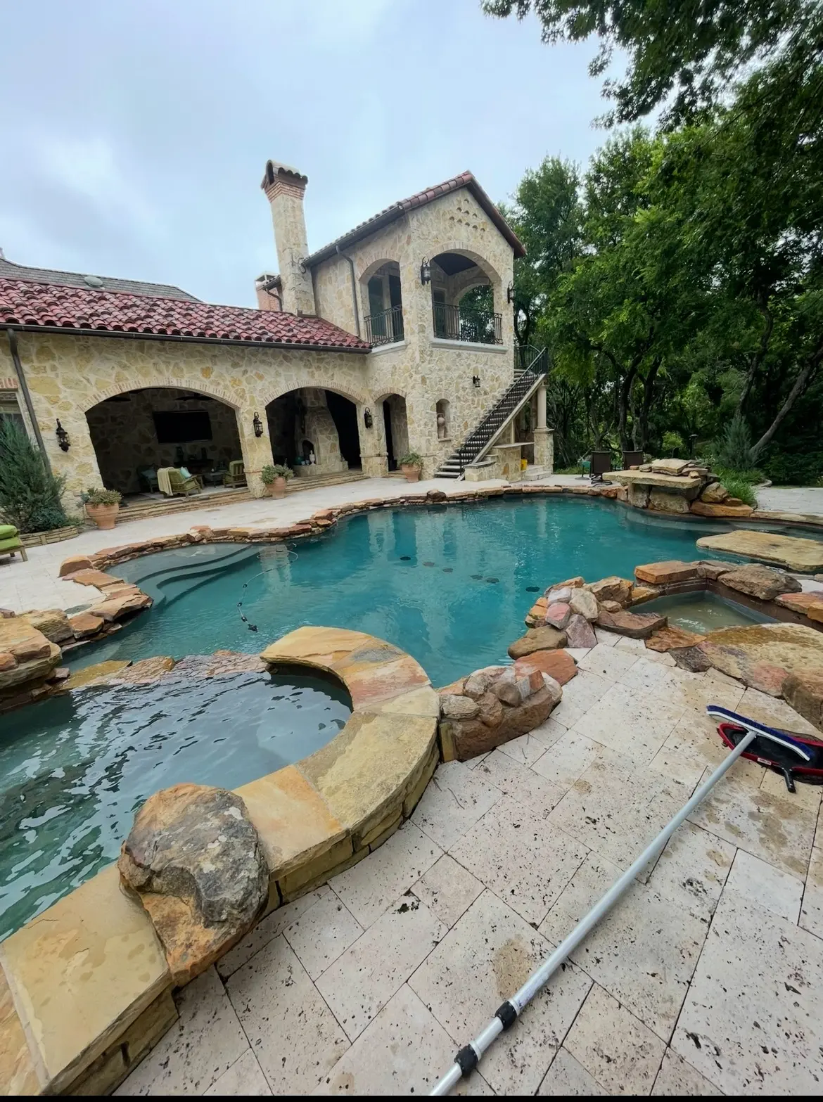 Mediterranean-style house behind a pool with a stone spa and waterfall
